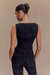 Détail du gilet en jean bleu foncé ajusté avec surpiqûres contrastées et bouton métal