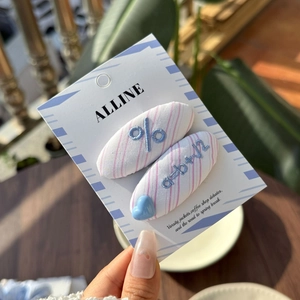 Detail of pink striped fabric hair clips with blue embroidery held in natural light