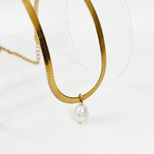 Detail of a golden flat snake chain necklace with a white teardrop pearl pendant