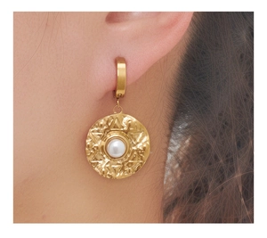 Close-up of golden irregular hammer-textured earrings with pearl inlay worn by a model