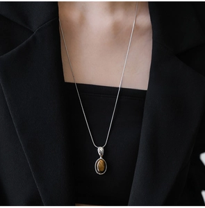 Detailed close-up of tiger eye stone pendant on a silver chain worn over black clothing