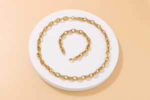 Detailed view of gold stainless steel anchor chain necklace and bracelet on white pedestal