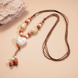 Gros plan d'un pendentif cœur en céramique blanche sur un collier en perles tressées