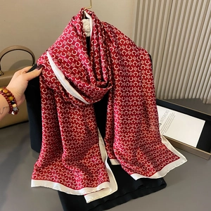 Silky red scarf with white monogram pattern and wide border displayed with accessories