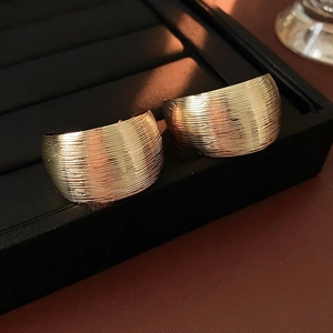 Detailed macro view of gold wide C-shaped hoop earrings with fine brushed metal texture