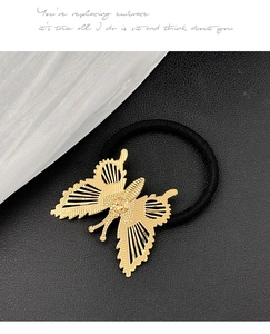 Detail eines goldenen Schmetterling-Haargummis mit verzierten Flügeln am schwarzen Seil