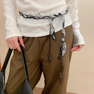 Detail of woven paisley silk scarf belt with wooden beads on a white shirt and brown pants