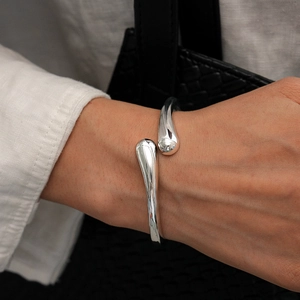 Macro detail of silver fluid waterdrop open cuff bracelet on a model's wrist