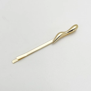 Detail view of a glossy gold irregular streamlined alloy hair clip on a neutral background