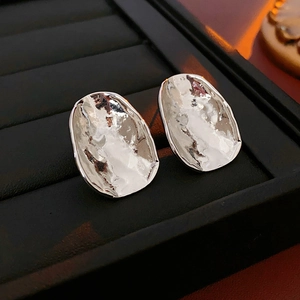 Macro shot of silver irregular oval metal earrings with hammered texture in a black gift box