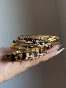 Close-up of leopard print leather and gold studded bangles stacked on a woman's wrist