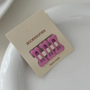 Detailed view of three purple bone-shaped hair clips on a cream-colored display card