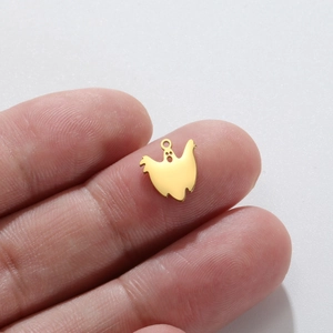 Polished gold stainless steel ghost pendant shown on a fingertip for size reference