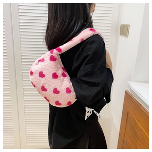 Side view of soft pink plush shoulder bag with heart patterns on a female model
