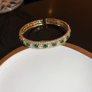 Detailed macro view of gold-plated bracelet with emerald green stones and white crystals