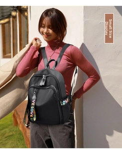 Outdoor shot of a black nylon backpack featuring a colorful 'LOVE' ribbon strap detail