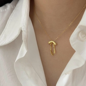 Detail of a gold bow pendant necklace on a model wearing a white shirt