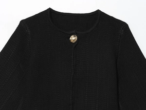Detail of black knit cardigan with close-up of golden metal button and woven texture