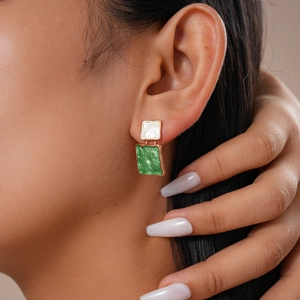 Close-up of geometric square earrings with white and green enamel in gold plating