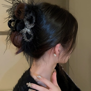 Detail of black feather and sparkling rhinestone bow hair claw clip for elegant hair buns