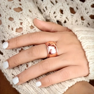 Close-up of polished rose gold wide band ring worn on finger with knit sweater background