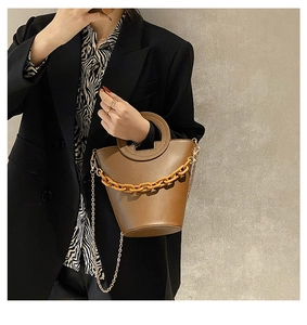 Detail of a brown bucket bag with ring handle and chunky resin chain worn by a model
