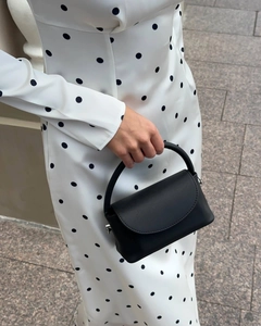 Detail of a black minimalist mini handbag paired with a French chic polka dot maxi dress