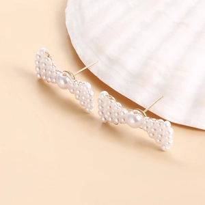 Macro detail of handmade pearl bow earrings placed on a white shell with soft lighting