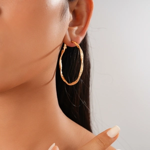 Detail showing the golden twisted texture of large hoop earrings on a model's ear