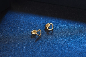 Macro view of polished gold heart stud earrings and matching backings on blue background