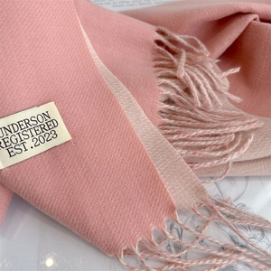 Close-up of pink cashmere-like scarf texture featuring tassels and a woven beige label