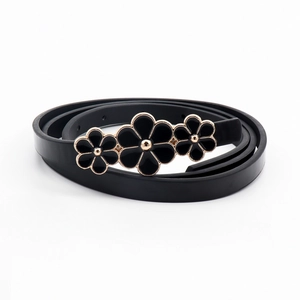 Detail of slim black leather belt featuring three golden rimmed flower buckles on white background