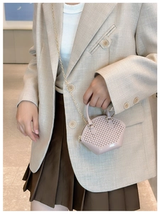Close-up of pink woven shell bag with metal chain strap held by a model in beige blazer