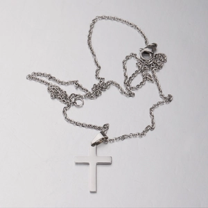 Close-up of silver cross pendant with mirror finish and lobster clasp on metal surface
