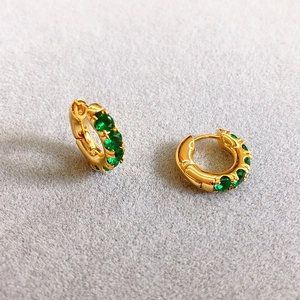 Close-up of 18K gold plated hoop earrings with green zircon stones on grey felt