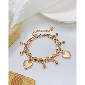 Layered gold heart bracelet with polished charms and round beads on a minimalist background