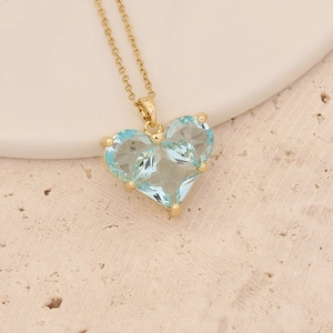 Macro shot of faceted ice blue heart pendant necklace with gold chain on stone texture