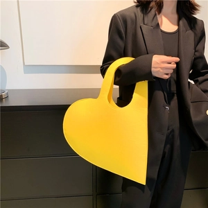 Minimalist bright yellow heart-shaped handbag held by a model in a stylish black suit