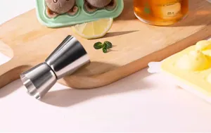 Polished stainless steel double jigger on wood board with lemon and mint leaves