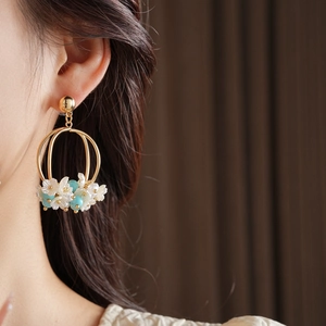 Close-up of golden hoop earrings featuring white flowers and light blue beads on a model