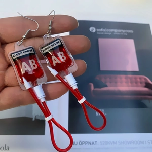 Close-up of creative Harajuku style blood bag earrings with AB blood group printed label