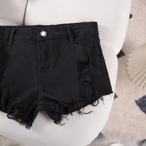 Detail shot of black distressed denim shorts featuring raw frayed edges and high-quality fabric