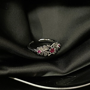 Macro view of silver star and flower ring with red gemstones on black silk fabric