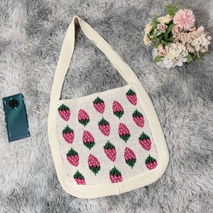Detailed flat lay of a knit strawberry tote bag with pink patterns on cream fabric