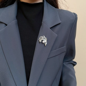 Dettaglio di un'elegante spilla a piuma con zirconi e perla indossata su un blazer scuro
