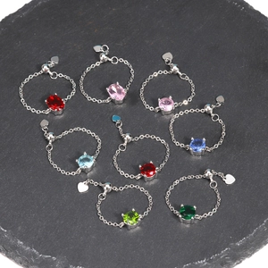 Detail of adjustable chain rings featuring various colorful zirconia gemstones on dark stone