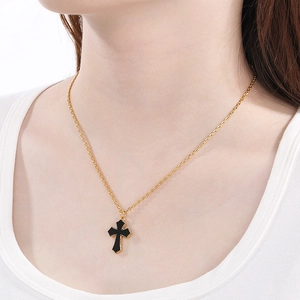 Gros plan d'un collier doré avec pendentif croix noire et détails perlés sur le cou