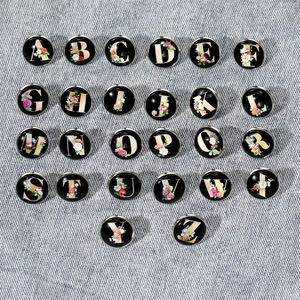 Flat lay of 26 floral alphabet charms from A to Z on blue denim fabric background