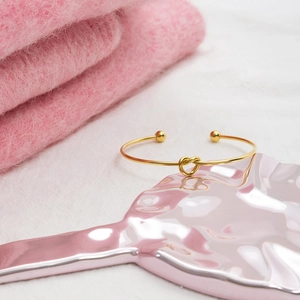 Classic 18K gold-plated stainless steel knotted heart open bangle on a pink display tray