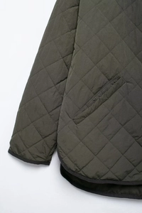 Detail of dark olive quilted jacket showing diamond stitch pattern and side pockets